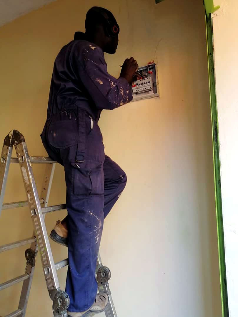 Technician on a ladder wiring a wall-mounted distribution board