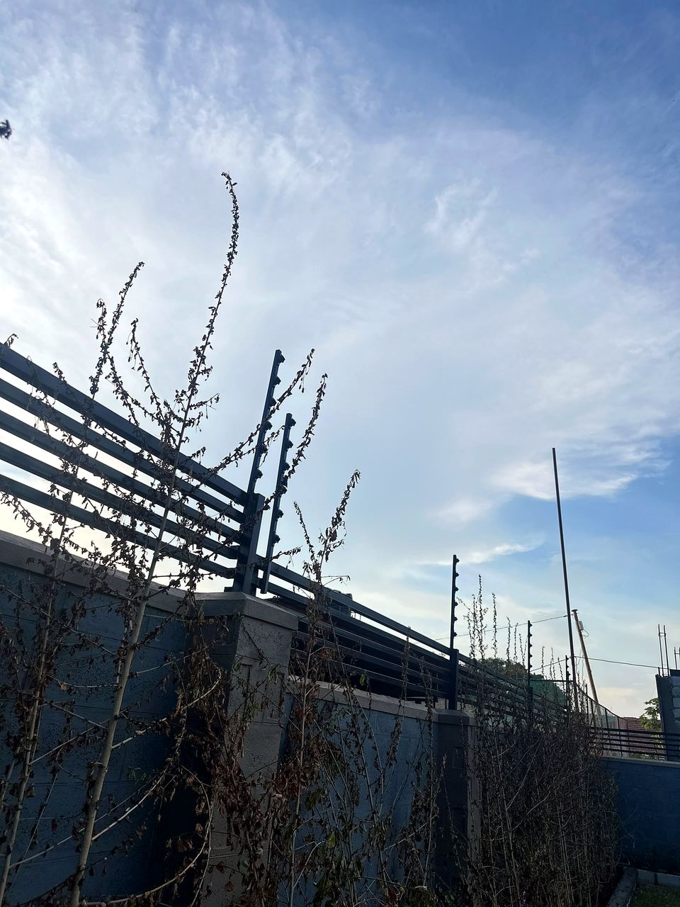 Electric fence brackets and wires on a slatted perimeter wall against a blue sky