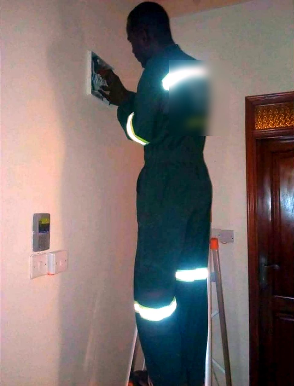 Technician in reflective overalls on a ladder working on an indoor distribution board