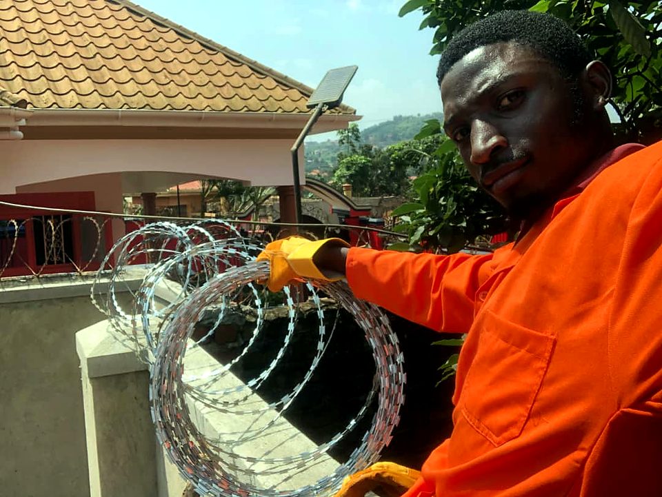 Technician in orange overalls and gloves installing razor wire on a compound wall